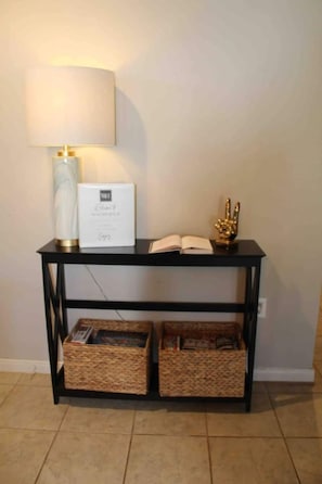 A black console table with a white lamp, a framed certificate, an open book, and two wicker baskets.