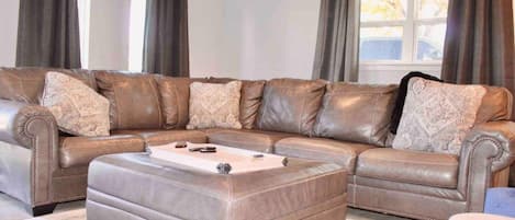 Een modulaire bank met bijpassend pouf in een woonkamer met een groot raam en gordijnen.