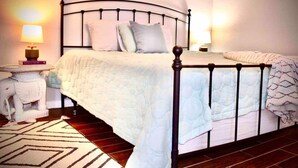 Un letto rifatto con un piumone bianco e cuscini, un comodino con una lampada e un tappeto decorato su un pavimento in legno.