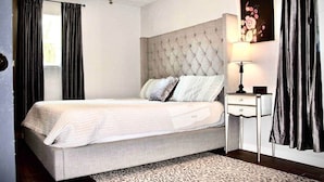 A bedroom with a tufted headboard, a bed with white bedding, a bedside table with a lamp, and a patterned rug. - 1BR Ranch Studio | Winery Escapes & Scenic Countryside Views (Saint Jo)