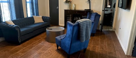 Un salon avec un canapé bleu, un fauteuil bleu, une table basse ronde et une cheminée.