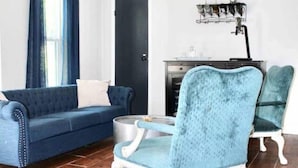 A living room with a blue sofa, a blue armchair, a coffee table, a ceiling fan, and a black door. - 1BR Ranch Studio | Winery Escapes & Scenic Countryside Views (Saint Jo)