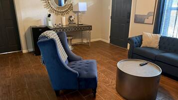Een woonkamer met een blauwe fauteuil, een ronde salontafel en een donkergrijze bank.