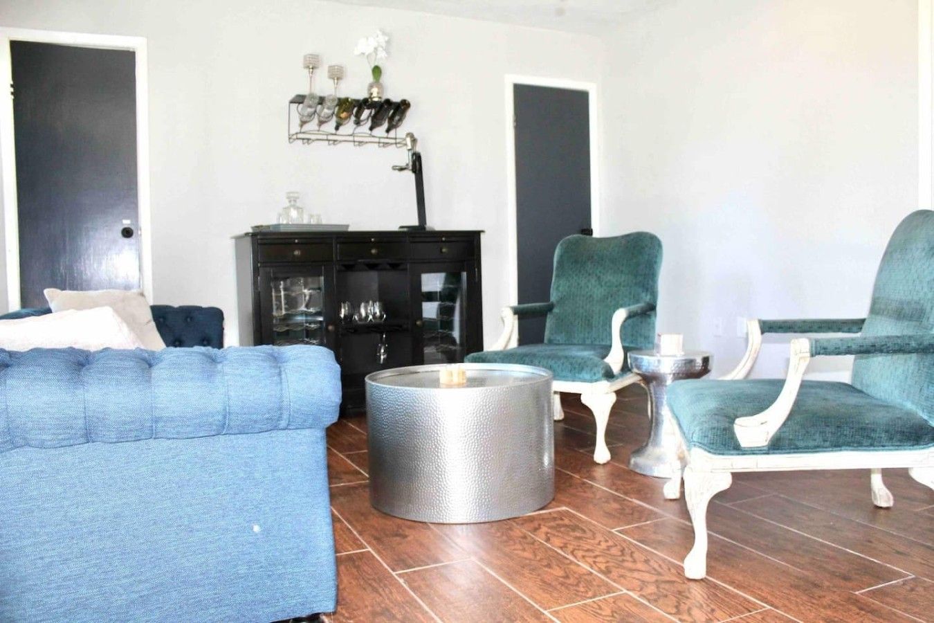 A living room with a blue sofa, two green armchairs, a round coffee table, and a black cabinet with glass doors.