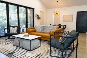 A modern living room with a sofa, armchair, coffee table, and a dining area with a table and chairs. - Stylish Nocona Barndo | Wineries + Fire Pit (Nocona)
