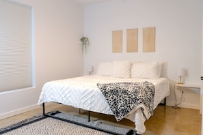 A bedroom with a bed, bedside tables, a window with blinds, and wall-mounted decor.