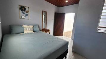 A bedroom with a large bed, a wooden ceiling, a small bedside table, a mirror, and a window.