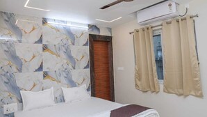 Una camera da letto con un letto, un ventilatore a soffitto, un condizionatore, una finestra con tende e un muro con effetto marmo.