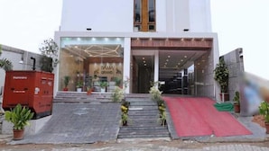 Un hotel moderno con facciata bianca, un elemento verticale centrale in legno e un tappeto rosso che conduce all'ingresso.