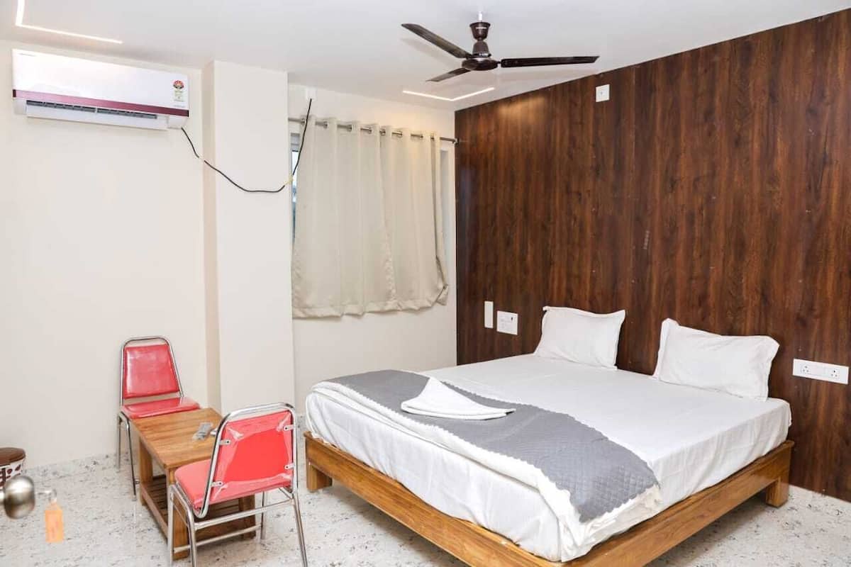 Egy hálószoba, melyben van egy fafejű ágy, fehér ágyneművel, egy mennyezeti ventilátor és egy kis asztal egy székkel.