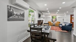 A modern living room with a dining area, featuring a large window, a fireplace, and a mounted picture of a street scene. - Enjoy the beautiful waters of Lake Couer d Alene all summer long! Only a few dates left in August and September!  Book now and enjoy all Cd'A has to offer!<br>A historically charming, newly renovated home in the heart of downtown Couer d Alene! (Couer d Alene)
