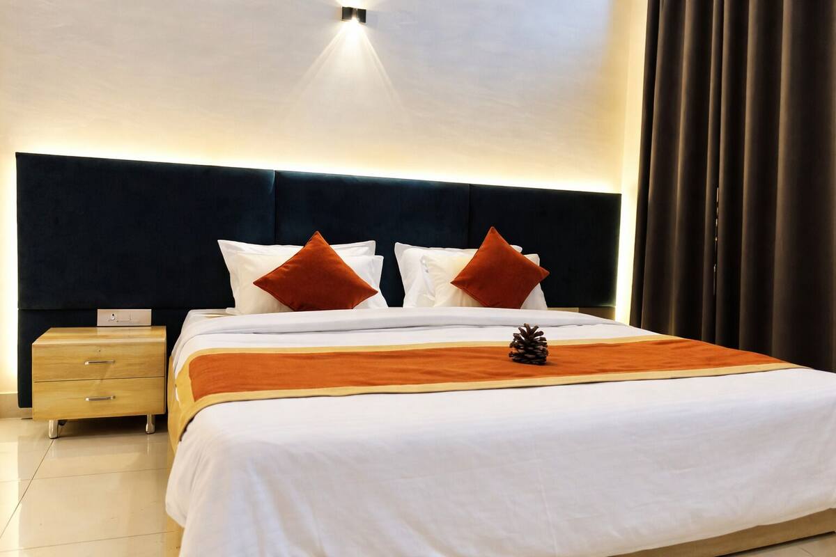 A neatly made bed with white linens, two red pillows, and a pine cone decoration.