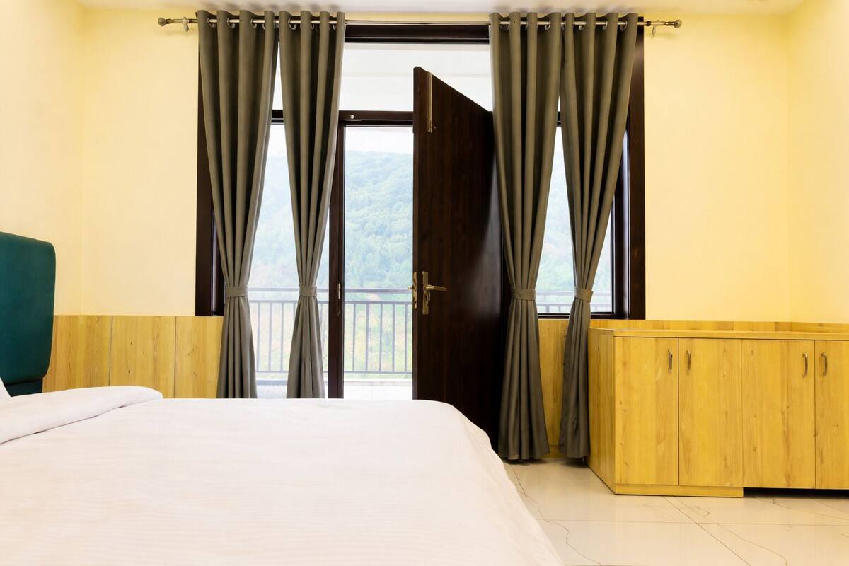 A bedroom with a bed, a wooden cabinet, and a balcony with curtains.