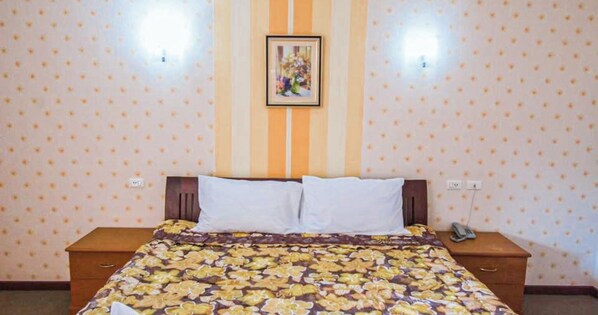 A bedroom with a floral bedspread, a wooden headboard, two bedside tables, and a wall-mounted light fixture. - Anchalee Garden Hotel (Wiang Sa)