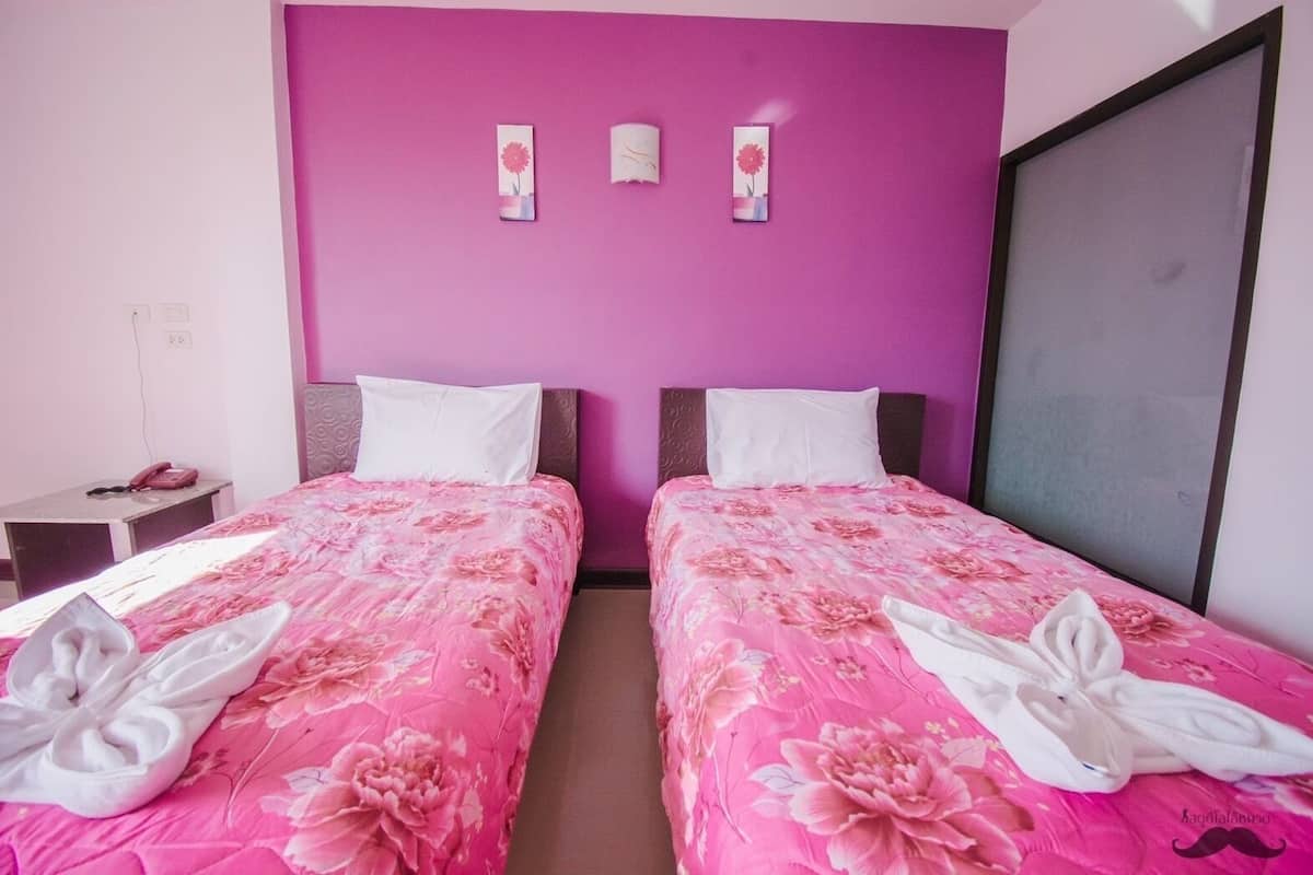A twin room with two beds, each with a pink floral bedspread and white pillows. There is a small bedside table with a pink telephone and a power outlet.