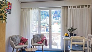 A hotel room with two armchairs, a small table, a bed, and a view of a snowy landscape through large windows.