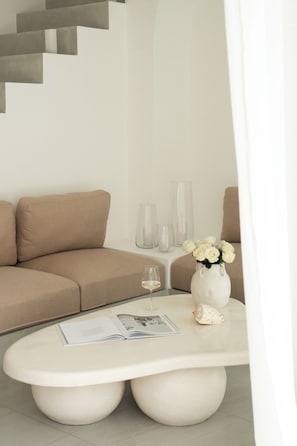 Una sala de estar moderna con un sofá color beige, una mesa de centro blanca con un jarrón de flores blancas y una copa de vino.
