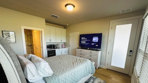 A bedroom with a bed, a TV, a desk, and a kitchenette.