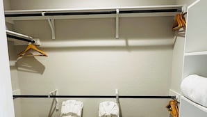 A walk-in closet with two black drying racks, a white towel shelf, and a wooden hanger rack.