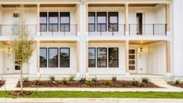 A two-story residential building with a symmetrical facade, balconies on each floor, and a well-maintained front yard.