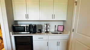 A compact kitchen with white cabinets, a black dishwasher, a microwave, a coffee maker, and a small sink.