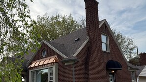 Ein Backsteinhaus mit großem Fenster, Schornstein und einem gepflegten Garten.