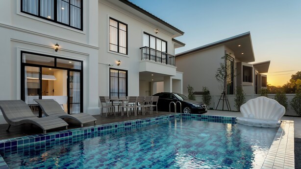 Une maison moderne à deux étages, dotée d’une piscine, d’un espace salon extérieur et d’une voiture garée à proximité.