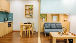 A compact living space with a kitchenette, a dining area, a sofa, and a small table with decorative items. - The Setai Apartments Linh Lang by XÔI Residences (Hanoi)