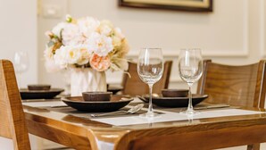 A dining table with two wine glasses, plates, and a vase of flowers. - The Setai Apartments Linh Lang by XÔI Residences (Hanoi)