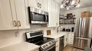A modern kitchen with white cabinetry, stainless steel appliances, and a wooden floor.