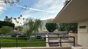 A balcony with a view of a parking lot, palm trees, and mountains.
