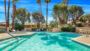 A clear blue pool surrounded by palm trees and lounge chairs.