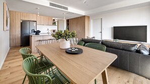 A modern kitchen with wooden cabinets, a built-in refrigerator, and a dining area with a wooden table and green chairs. - Margaret's Luxe Apartment (Margaret River)
