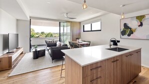 A modern kitchen with a large island, wooden cabinets, and a dining area with a table and chairs. - Margaret's Luxe Apartment (Margaret River)