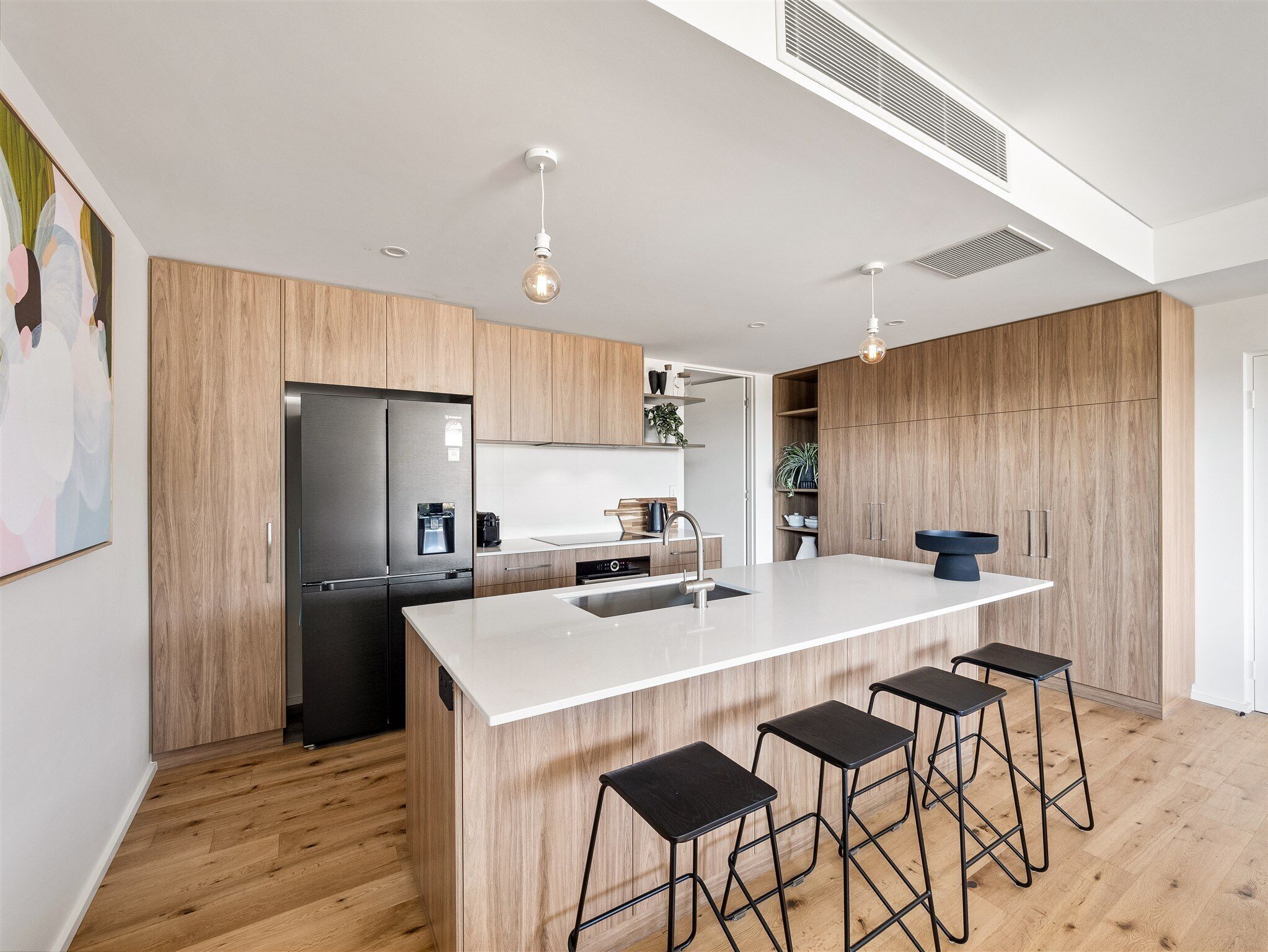 A modern kitchen with a large island, wooden cabinets, stainless steel appliances, and bar stools.