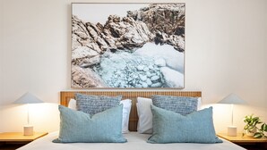 Una cama con una colcha de diseño azul y blanco, dos almohadas a juego y una fotografía enmarcada de un paisaje rocoso.