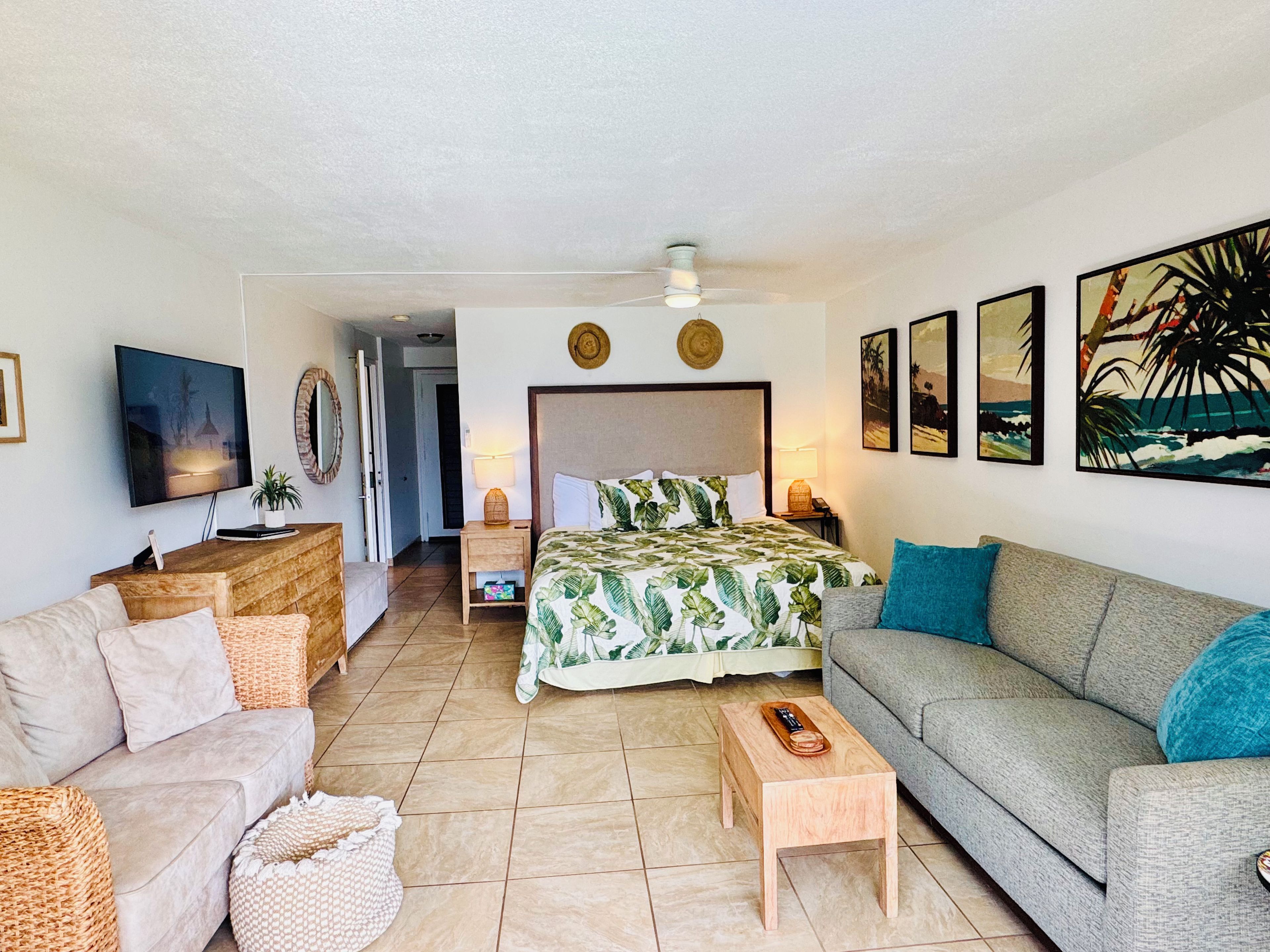 Une chambre d’hôtel avec un lit, un canapé, une télévision et des œuvres d’art accrochées aux murs.
