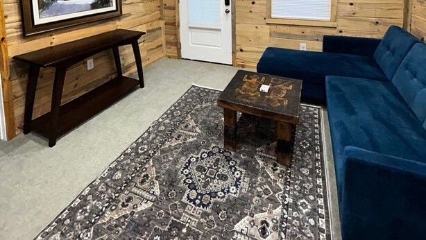 Una habitación acogedora con paredes de madera, un sofá azul, una mesa de centro de madera oscura, una alfombra estampada y un cuadro en la pared.
