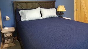 Una cama con cabecera de madera, dos almohadas, una lámpara de noche y una mesita de noche.