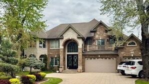 A two-story house with a brick facade, a large garage, and a driveway leading to the entrance. - Luxury 5BR Family Getaway – Heated Pool, Hot Tub, Fire pit, Game Room, (Roselle)
