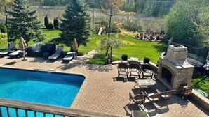 A backyard with a swimming pool, lounge chairs, a barbecue area, and a stone fireplace. - Luxury 5BR Family Getaway – Heated Pool, Hot Tub, Fire pit, Game Room, (Roselle)