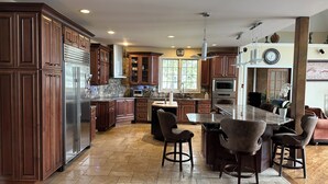 A spacious kitchen with wooden cabinets, a central island, and a dining area with bar stools. - Luxury 5BR Family Getaway – Heated Pool, Hot Tub, Fire pit, Game Room, (Roselle)