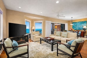 A spacious living room with a large flat-screen TV, comfortable seating, a coffee table, and a view of the ocean. - Hale Moana Kai: A stunning 2-bedroom ocean view condo in Kailua Kona. (Kailua-Kona)