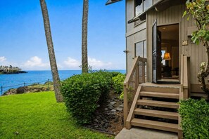 A coastal property with a wooden staircase leading to a door, a view of the ocean, and a well-maintained lawn.