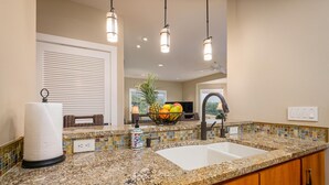 A kitchen with granite countertops, a white sink, wooden cabinets, and a fruit bowl on the counter.