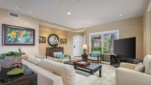 A spacious living room with a sofa, coffee table, and TV. There is a fireplace, artwork on the wall, and a large window.