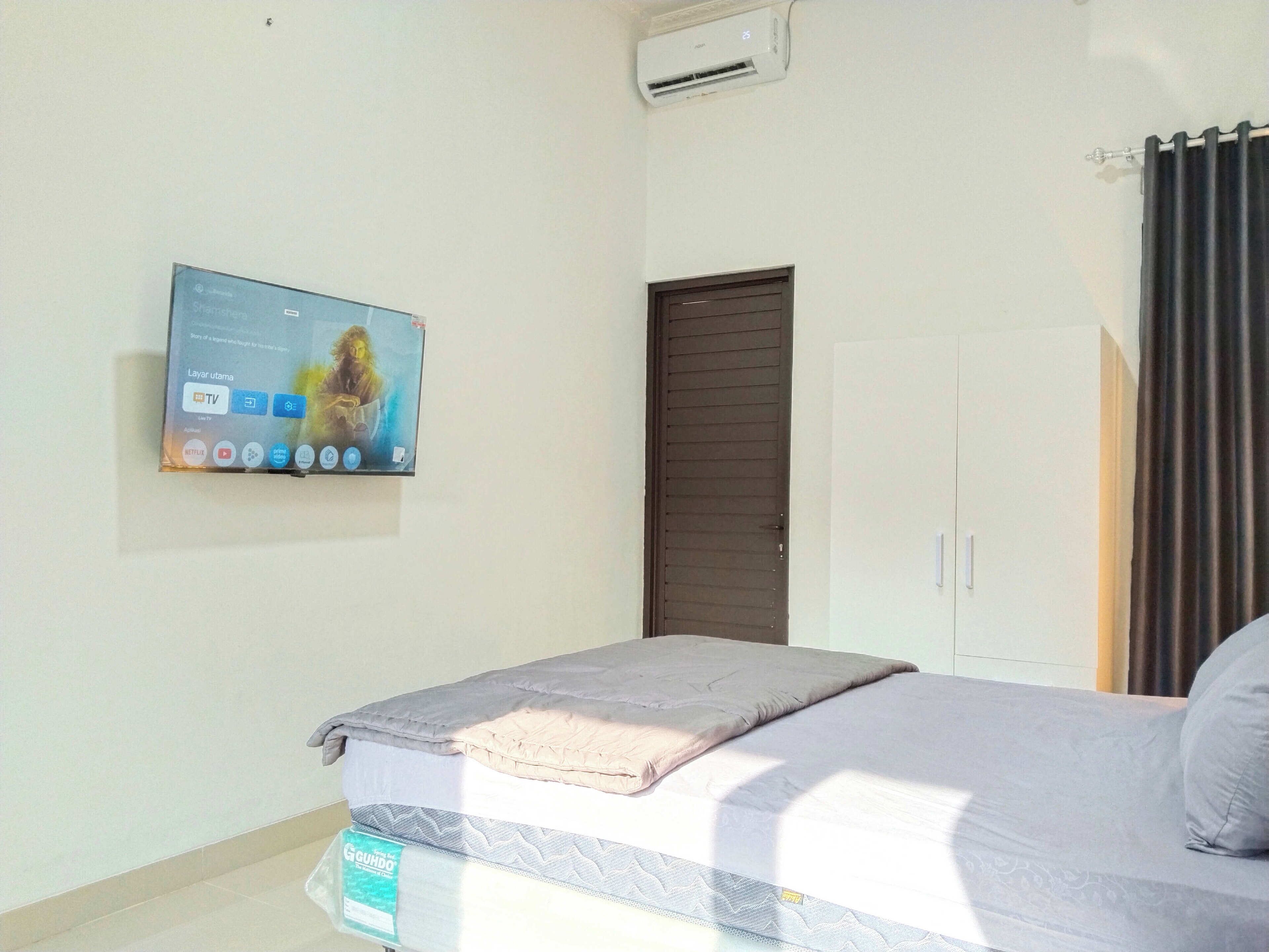 Una camera da letto con un letto, una TV a parete, una porta e una finestra con tende.