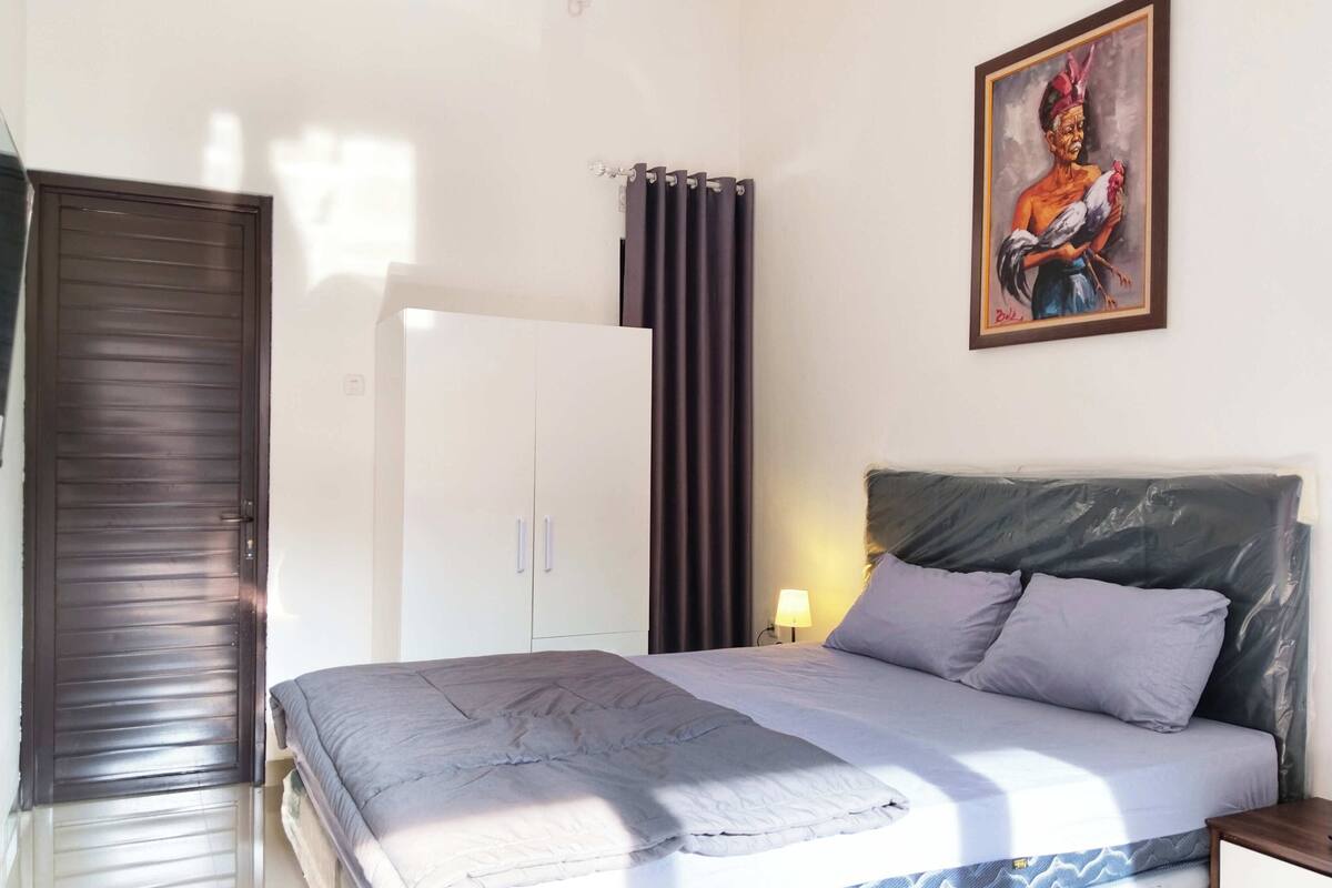 Een slaapkamer met een bed, een kledingkast, een schilderij en een gordijn.