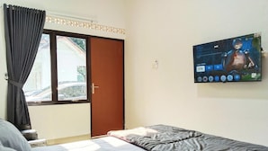 Une chambre avec un lit, un téléviseur fixé au mur et une fenêtre avec des rideaux.