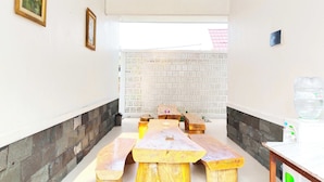 Un espace repas avec des bancs et des tables en bois, un mur en pierre et une grande fenêtre.